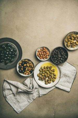 A variety of olives in bowls on concrete background with linen, copy space
