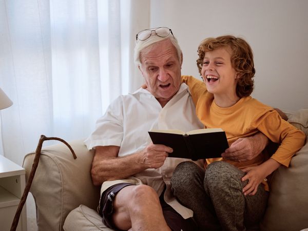 Cheerful boy and grandfather with book on couch