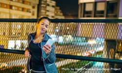 Portrait of young woman runner listening music on mobile phone application in evening bYqPkD