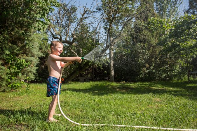 Little child having fun with garden hose and water