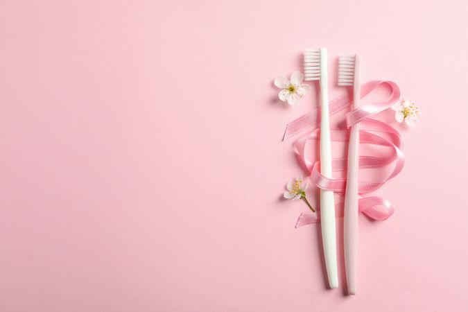 Toothbrushes, ribbon and flowers on pink background, space for text