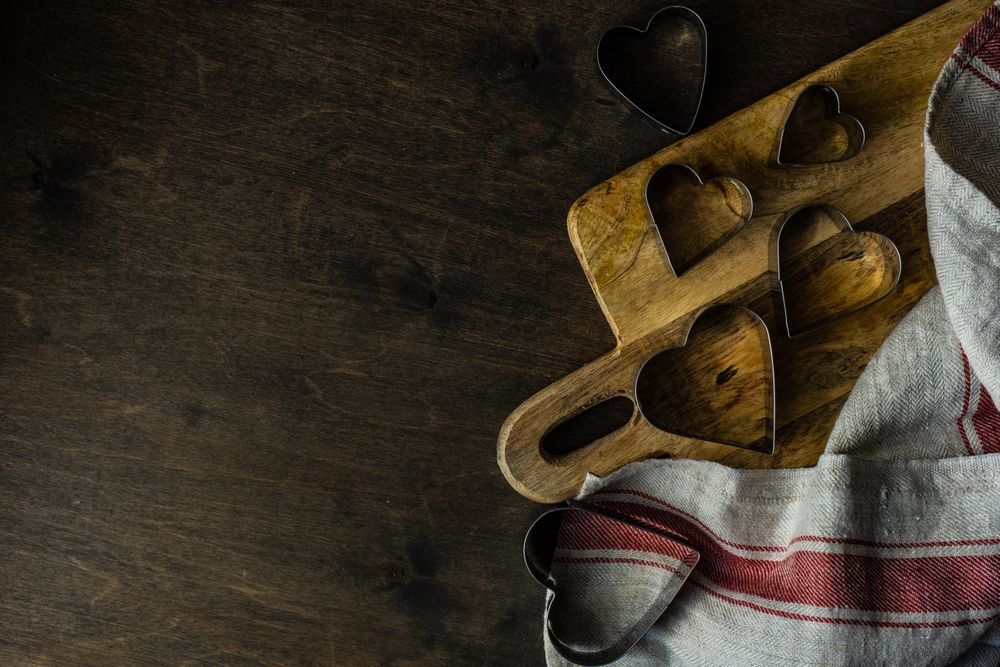 Heart shaped cookie cutters on wooden cutting board with kitchen towel with copy space