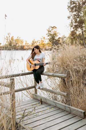 Young woman playing guitar near water