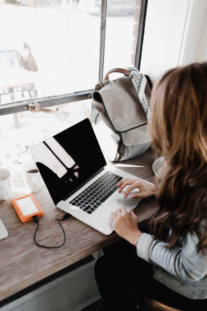 Woman working on a laptop sitting at a table near window