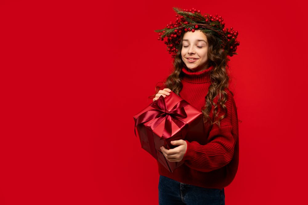 Teen girl wearing Christmas berry wreath holding red gift box.