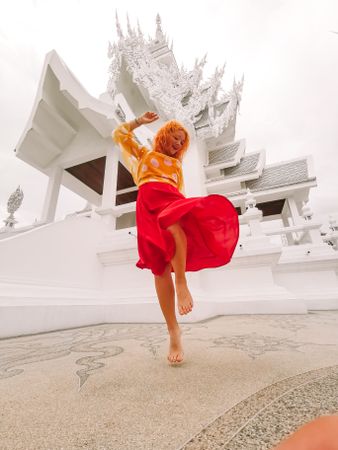 Low angle view of a dancing woman in red skirt standing beside light temple