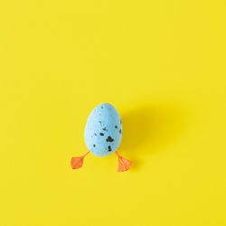 Blue egg with duck legs on yellow background