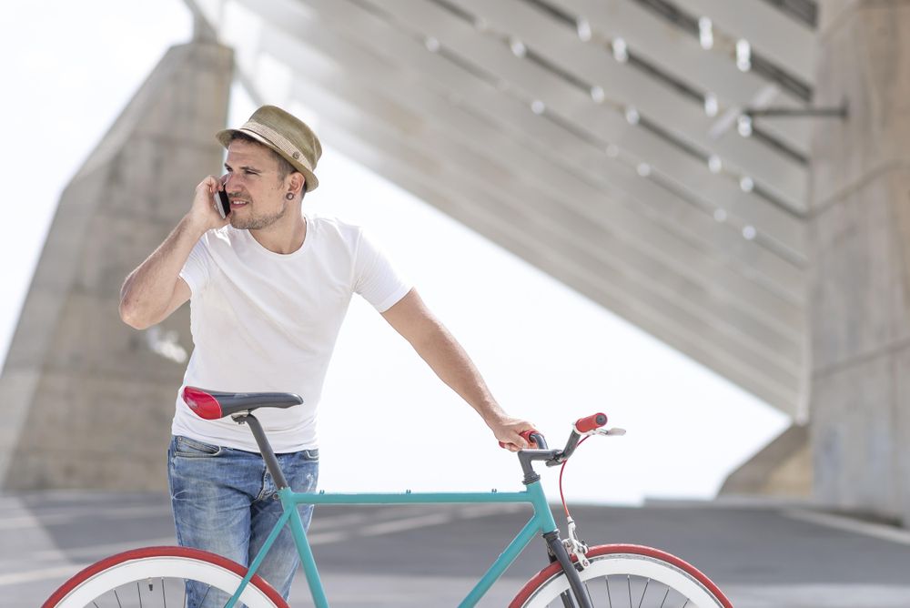 Male with bicycle talking on phone under modern building