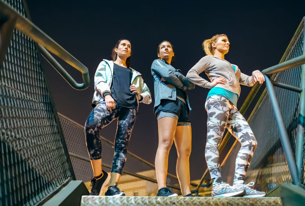 Three women standing on stairs at night ready for an evening exercise session in the city