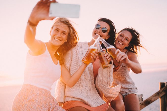 Group of young women taking a selfie at the beach with beers