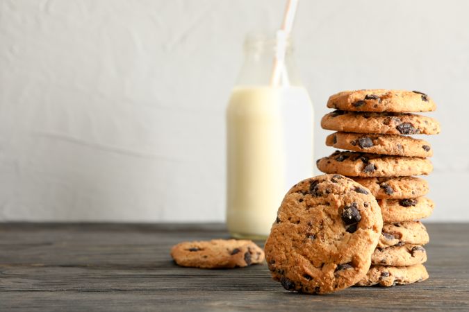 Tasty chocolate chip cookies and bottle of milk on wooden table. Space for text