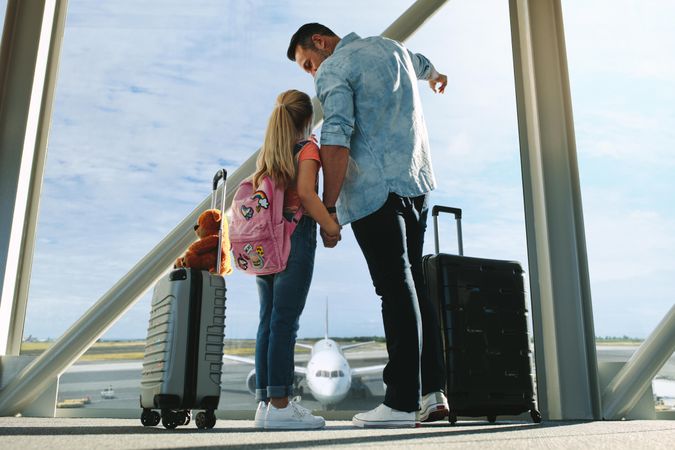 Man showing a plane to her daughter while waiting at airport terminal
