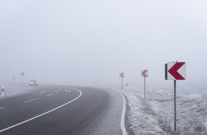 Dangerous road curve and warning signs in a dense mist