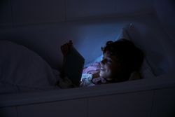 Child browsing tablet in bathroom with lights off