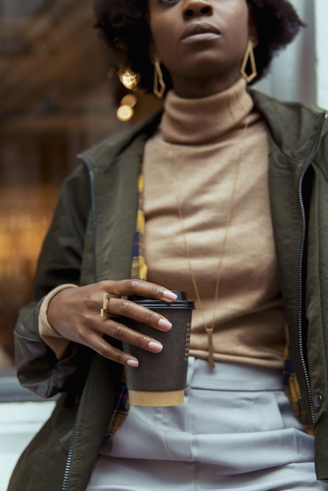 Close-up shot of Black woman in green jacket holding a cup of coffee