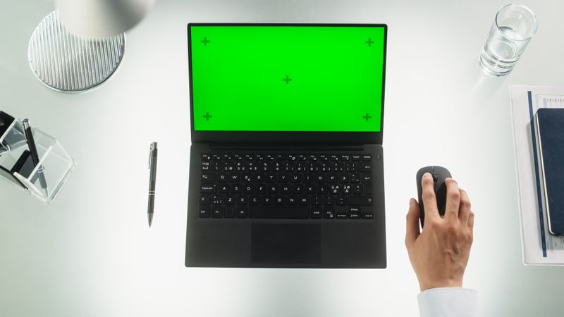 Anonymous Corporate Employee Using Laptop Computer with Mock Up Green Screen Chromakey Display with Placeholders. Man Sitting Behind a Desk, Browsing Internet, Using a Wireless Mouse. Top Down View