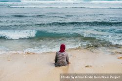 Back of Muslim woman sitting at water's edge on Bali beach 0PxMl0