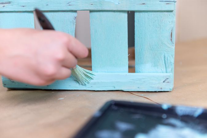 Woman paining wooden box in blue color with brush