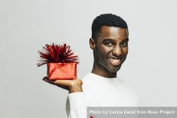 Smiling Black man holding up a present wrapped in red 4jpKW0