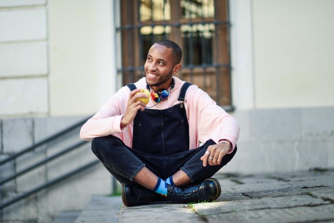 Confident male in overalls and boots sitting cross legged on outdoor steps