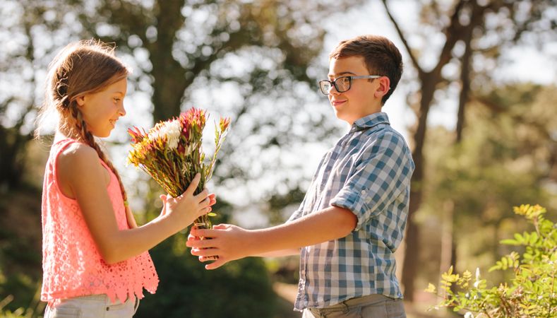 Boy giving flowers to a girl standing in a park