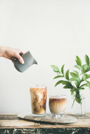 Hand pouring cream from grey pitcher into iced coffee, copy space