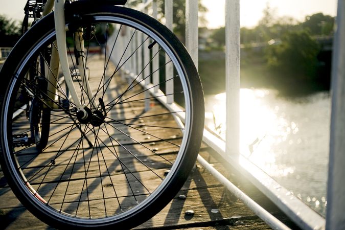 Wheel of bike on bridge looking down at sun on water