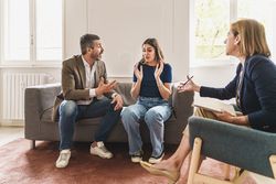 A married couple heatedly argue on a couch during a therapy session