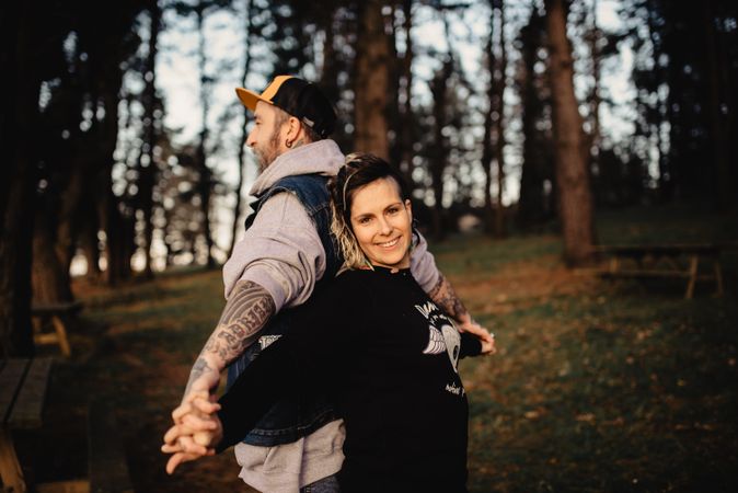 Young guy and happy woman standing back to back in forest