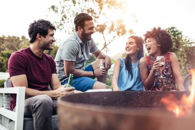 Group of young men and women enjoying drinks together around fire pit