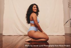 Smiling young woman kneeling in blue underwear against a studio background 4Now2b