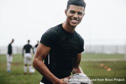 Portrait of a smiling footballer standing on field in rain bGKAab