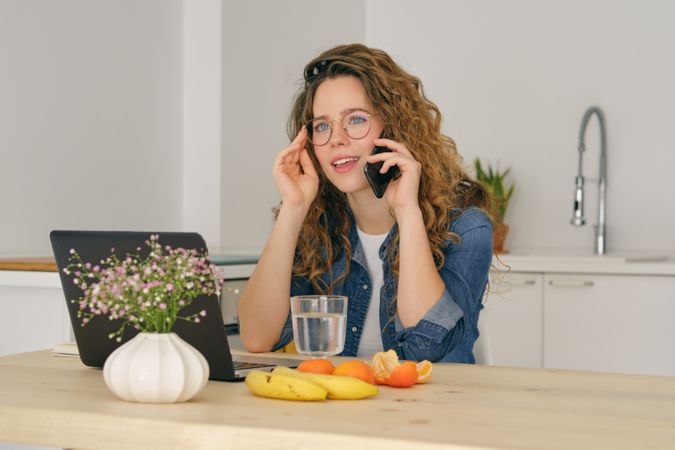 Thoughtful woman talking on smartphone in kitchen