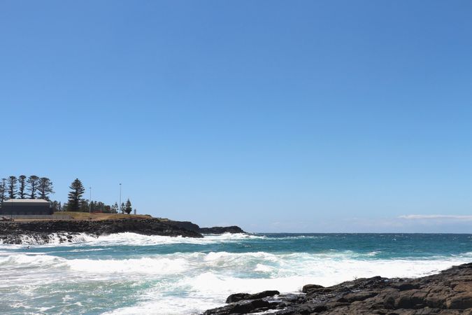 Waves crash against rocky shore under bright blue sky in coastal landscape