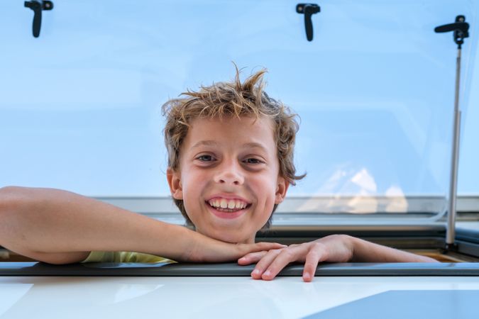 Delighted boy looking at camera from camper window
