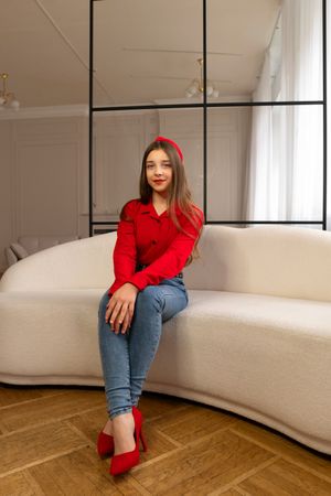 Teen girl sitting on beige sofa wearing red outfit.