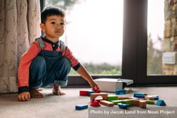 Sweet little boy sitting on floor with colorful wooden blocks lying in front 4d7MQ5