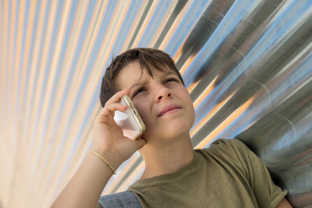 Serious boy talking on smartphone leaning on metal wall
