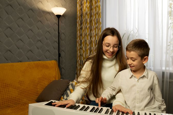 Teen girl and boy smiling while playing piano together
