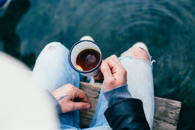 Top view of man holding coffee while sitting on pier