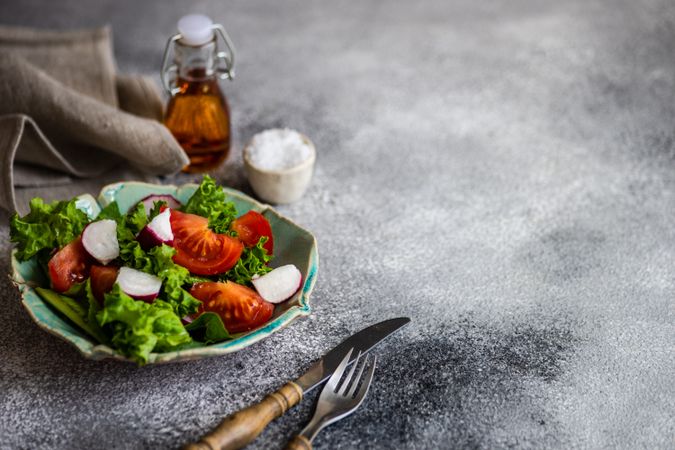 Bowl of salad with tomatoes, radish & lettuce on grey counter with space for text