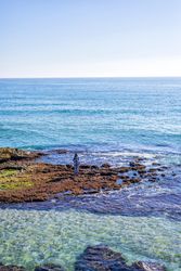 Female dressed in blue standing on coastal rocks near water