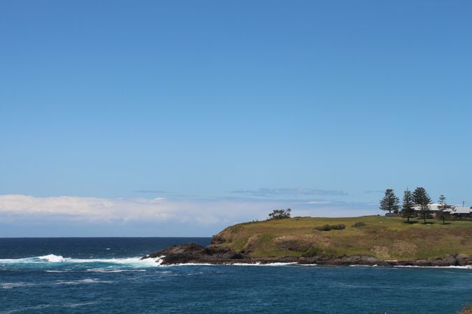 Scenic coastal view featuring a grassy landform and gentle ocean waves under a clear blue sky near the shore