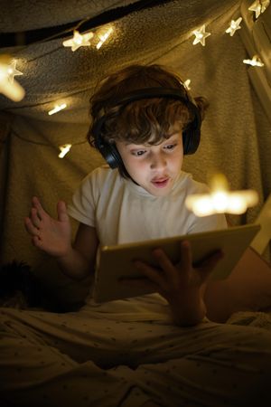 Excited boy watching video on tablet in blanket fort