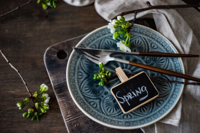 Spring table setting with blossom and cutlery on blue patterned plate