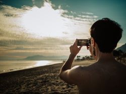 Tourist taking photo of sunset on beach