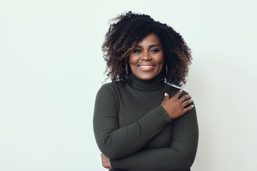 Happy Black woman looking at camera with her hand on her shoulder