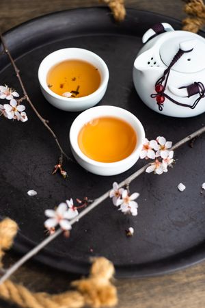Cups of green tea and pot with floral petals
