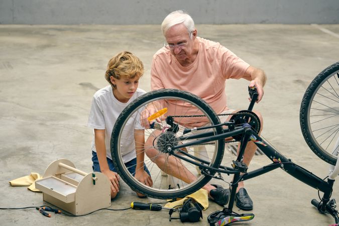 Mature man repairing bicycle wheel with grandson