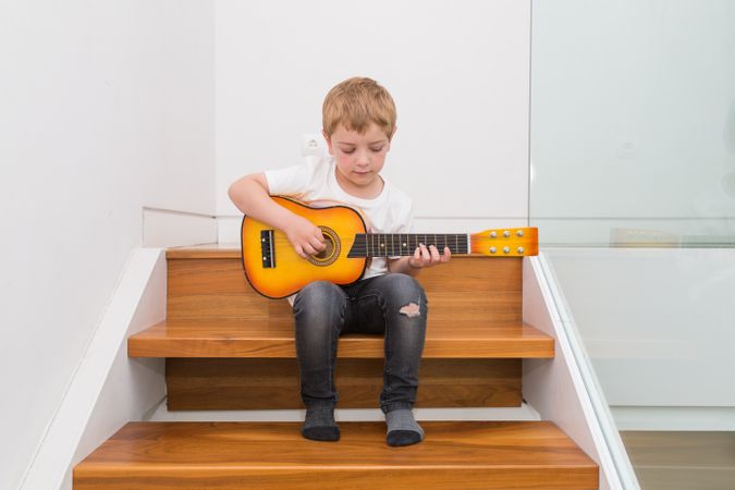 Young blonde boy playing toy guitar